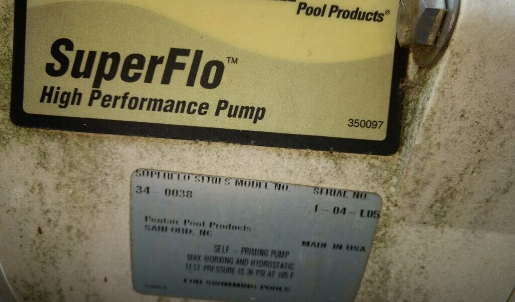 Close-up of a Pentair SuperFlo high performance pump label showing model number 34-0038. The label reads Pentair Pool Products, Self-Priming Pump, Made in USA, with specifications such as 155 PSI and 150°F. Some dirt is visible on the surface.