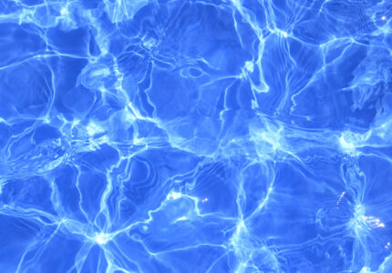 Clear blue water with sunlight creating ripples and reflections on the surface. Waves and patterns form abstract designs, showcasing the natural movement and play of light.