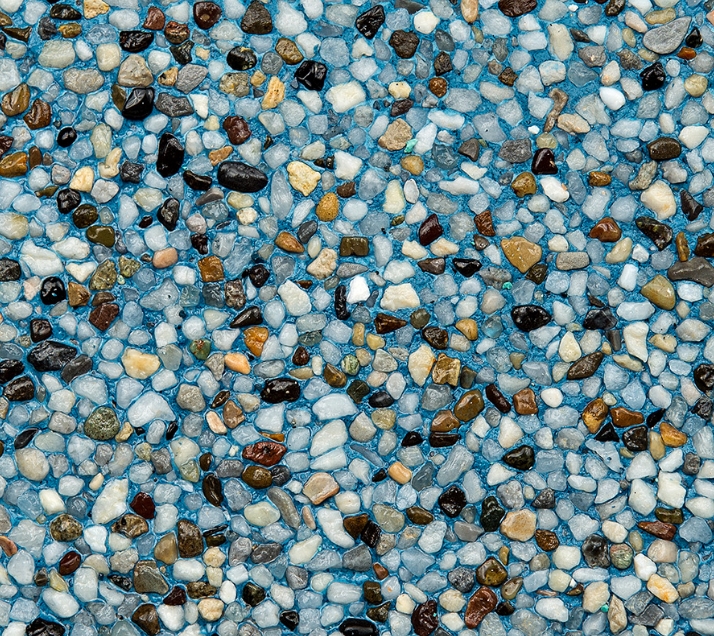 A mosaic of small, multicolored pebbles embedded in a light blue background, creating a textured and vibrant surface. The stones vary in shades of brown, black, white, and gray, presenting a natural and earthy pattern.